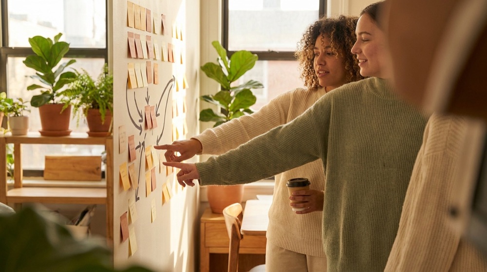 Two people mapping a process on a wall of warm-toned sticky notes.